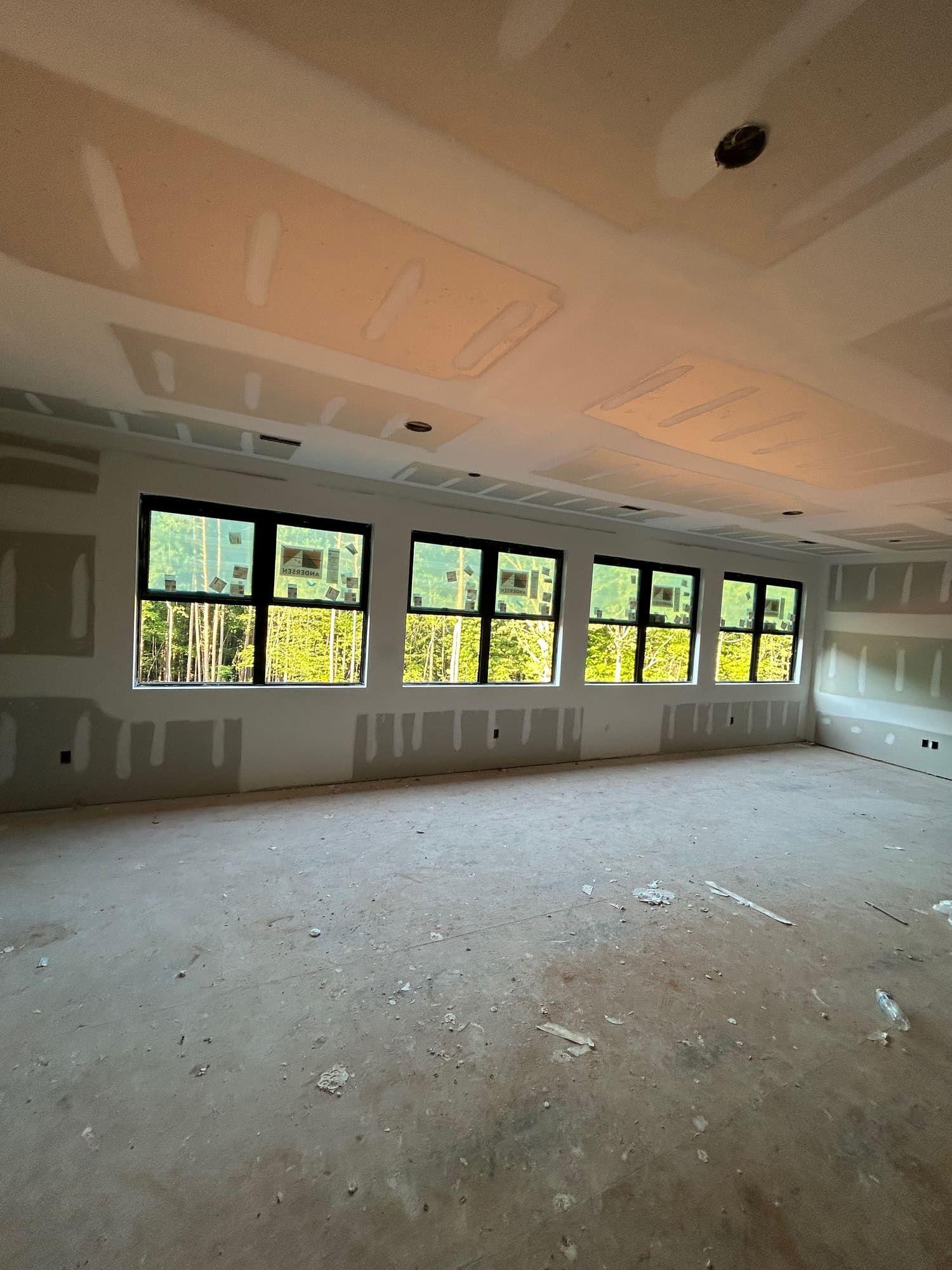 Large room with wall of windows, drywall finishing complete before paint