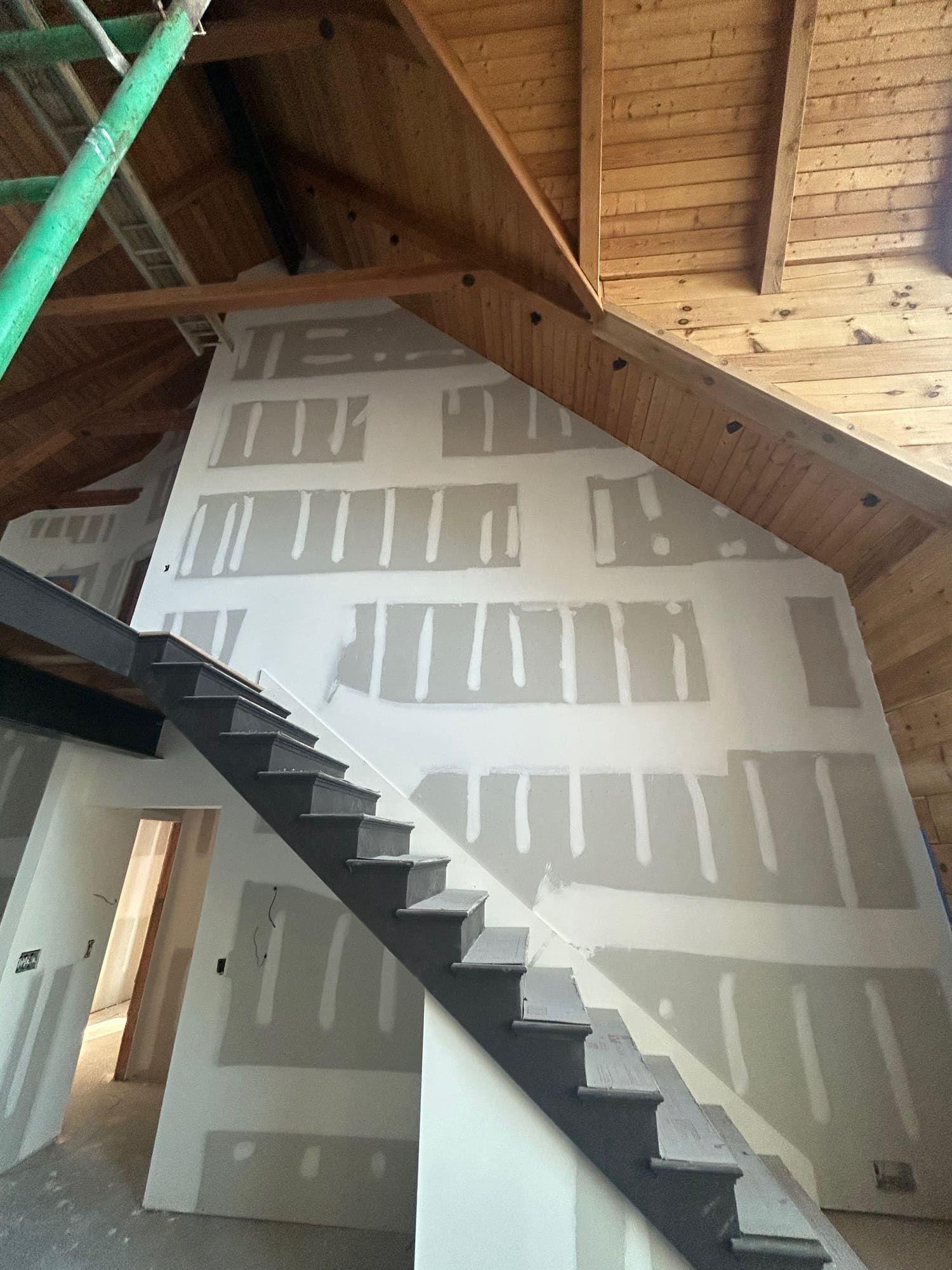 Drywall taping on angled staircase wall under vaulted wood ceiling