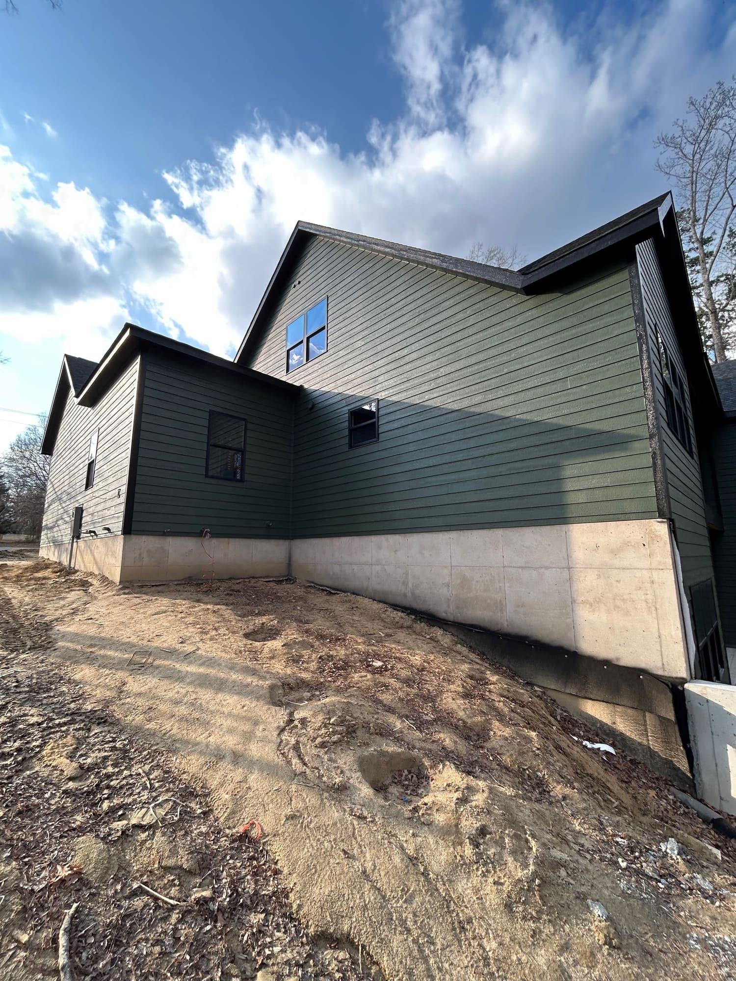 Green and black exterior siding paint job, side elevation with stone foundation