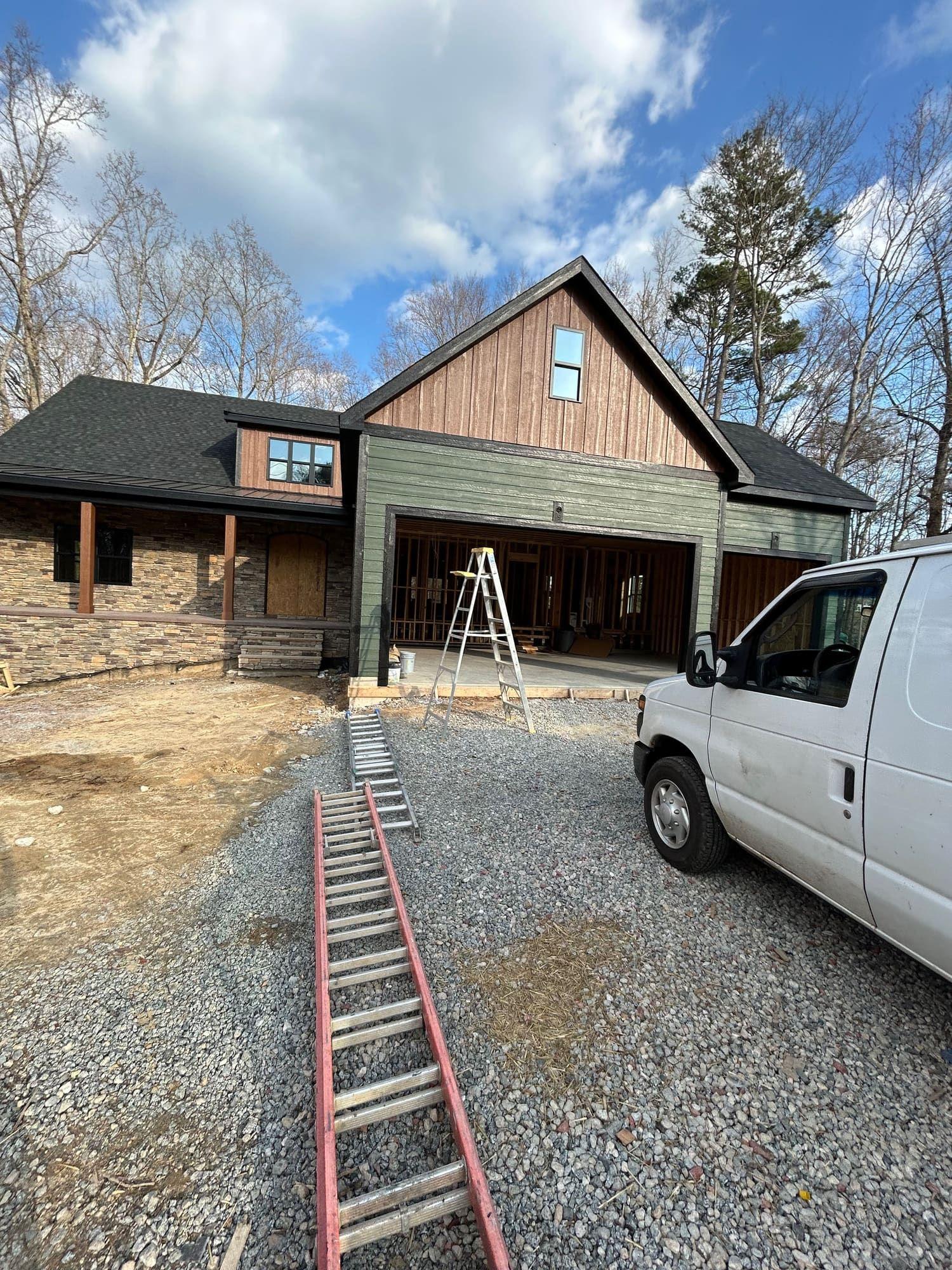 Exterior paint job in progress with ladders and equipment, garage and gable